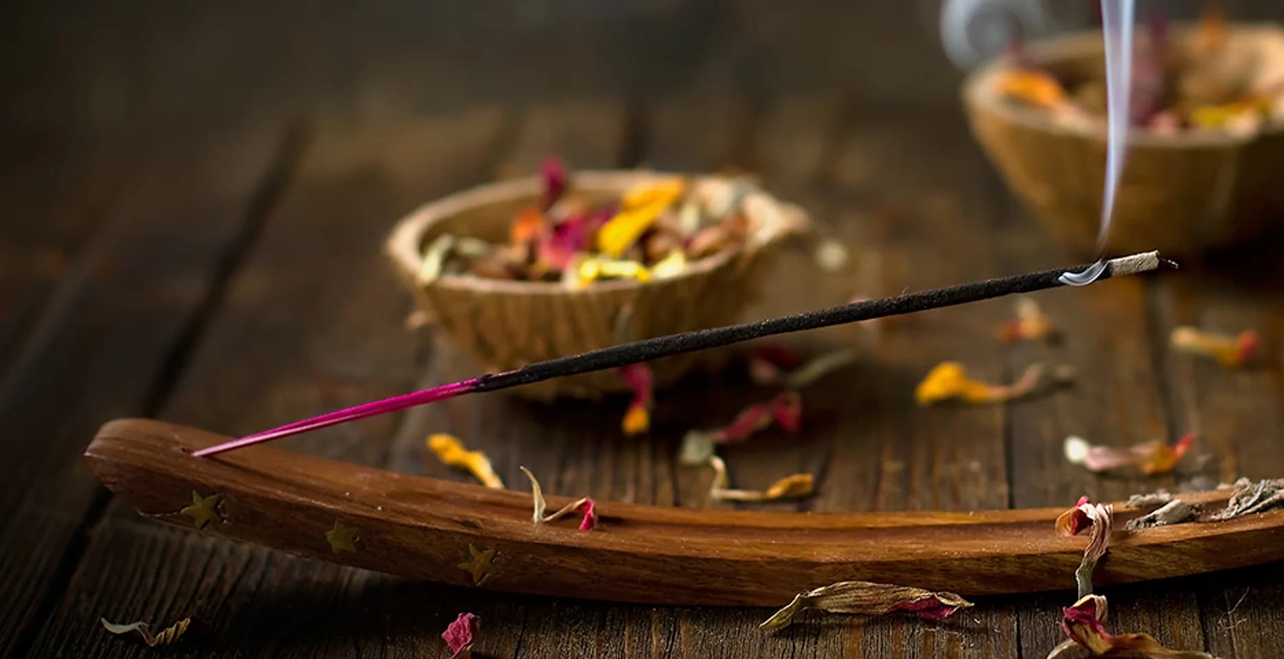 A lit incense stick on a wooden holder, with dried flower petals around it