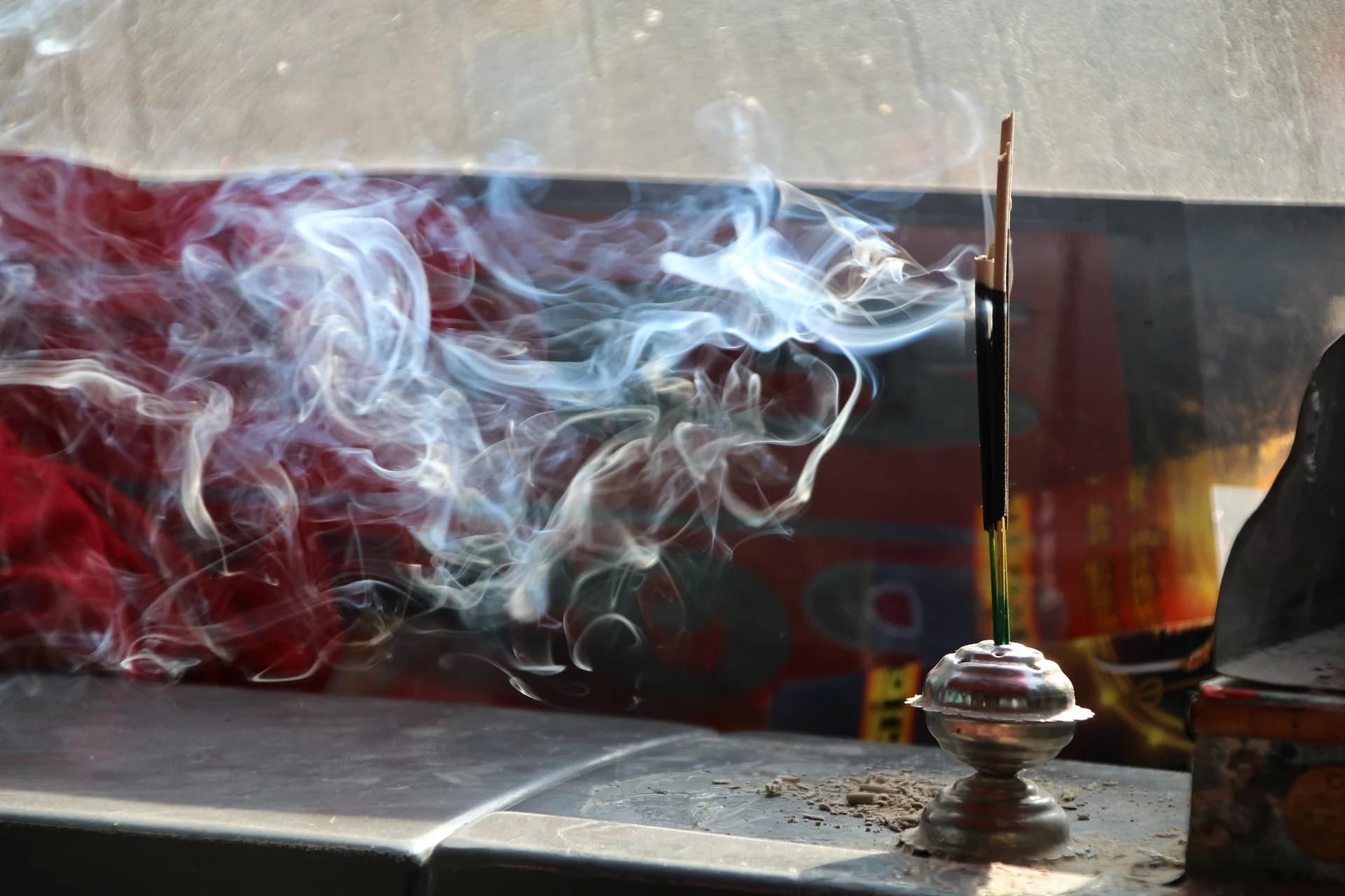 Incense smoke curling against a red temple wall
